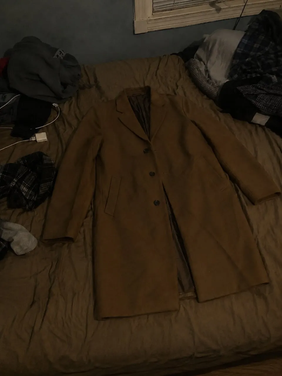 A poor listing photo: a coat on a messy bed in dim light with clutter in the background