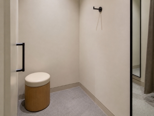 A neutral fitting room with a hook, stool and mirror